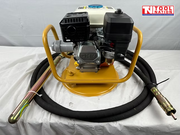 Petrol engine in a yellow cradle with coiled black hose, metal vibrator head, coupling, and logo in the top corner.
