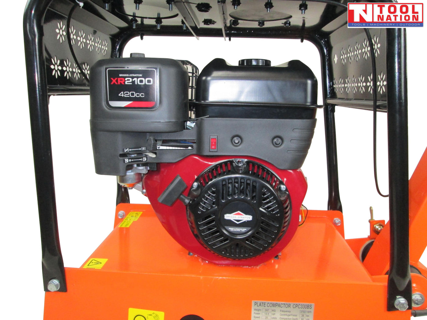Close-up of the petrol engine on an orange plate compactor with black protective frame, fuel tank, pull start, warning labels, and logo in the top corner.