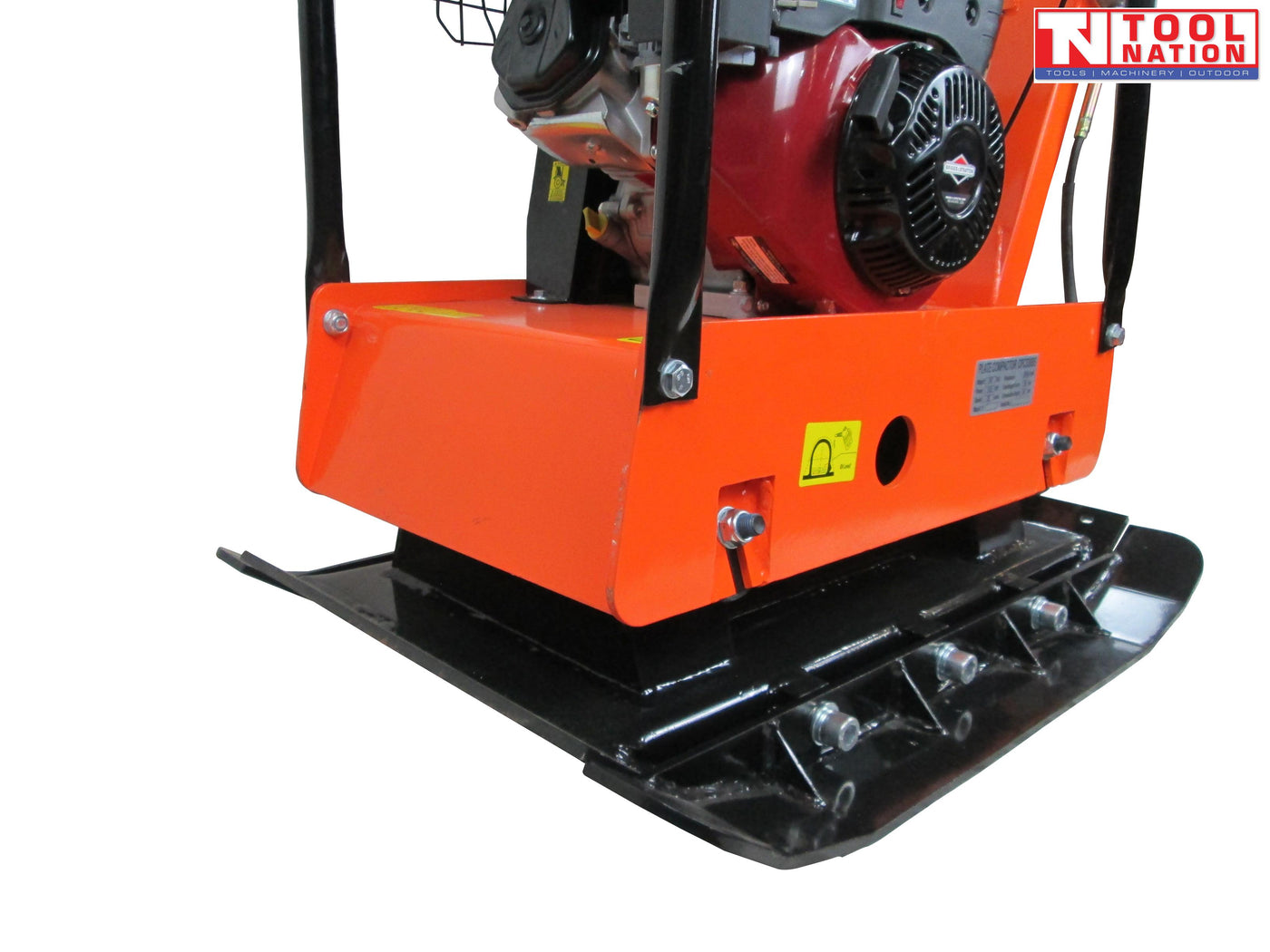 Close-up angled view of an orange plate compactor showing the petrol engine, protective frame, black base plate, bolts, warning labels, and logo in the top corner.