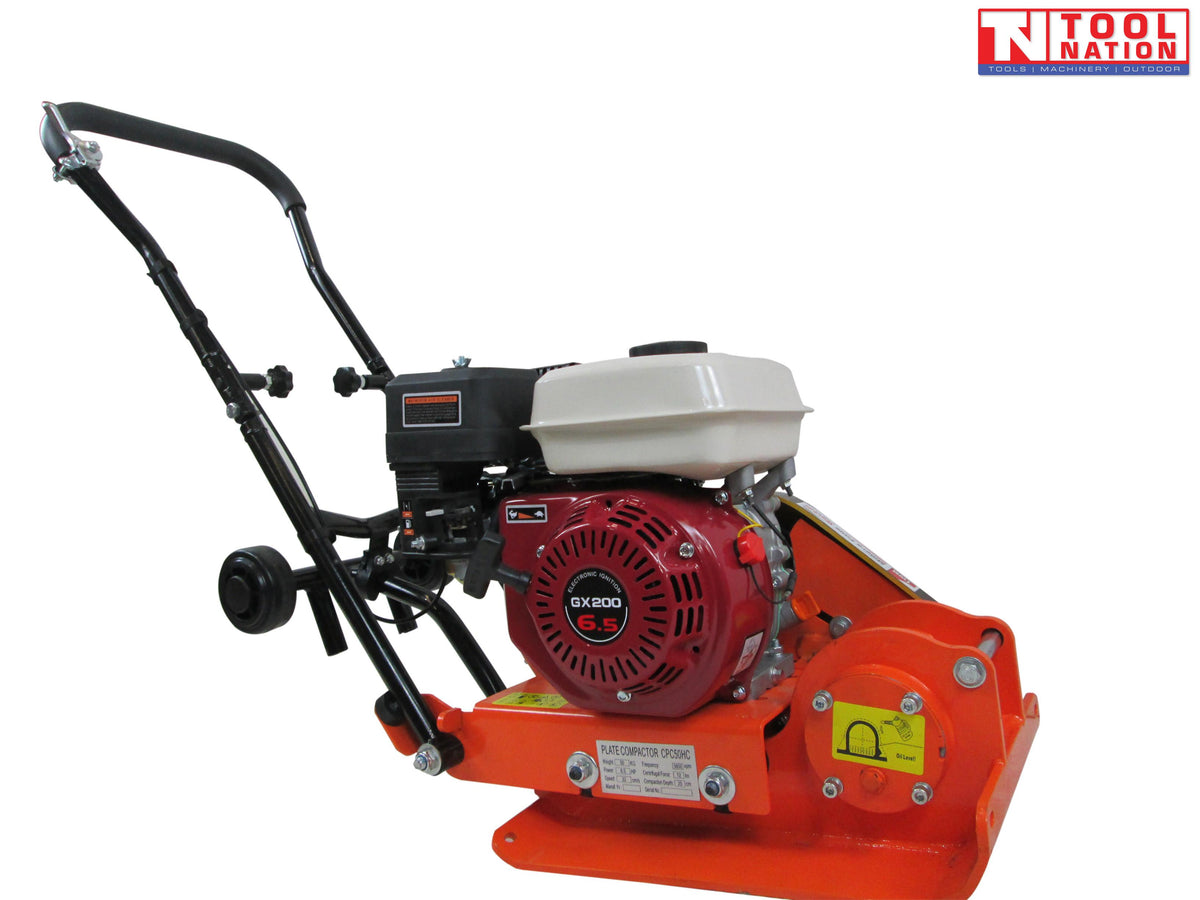 Orange plate compactor with petrol engine, black handle, wheels, base plate, warning labels, and logo in the top corner.
