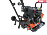 Close-up angled view of an orange plate compactor showing the petrol engine, wheel kit, handle frame, base plate, and logo in the top corner.