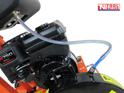Close-up of a petrol engine on an orange floor saw with water hose, blade guard, warning label, and logo in the top corner.