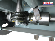 Close-up underneath a floor saw showing a greased gear mechanism, metal shaft, bolts, and grey frame.