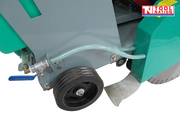 Close-up of a floor saw lower side showing a wheel, clear hose, valve, blade guard, diamond blade, and grey frame.