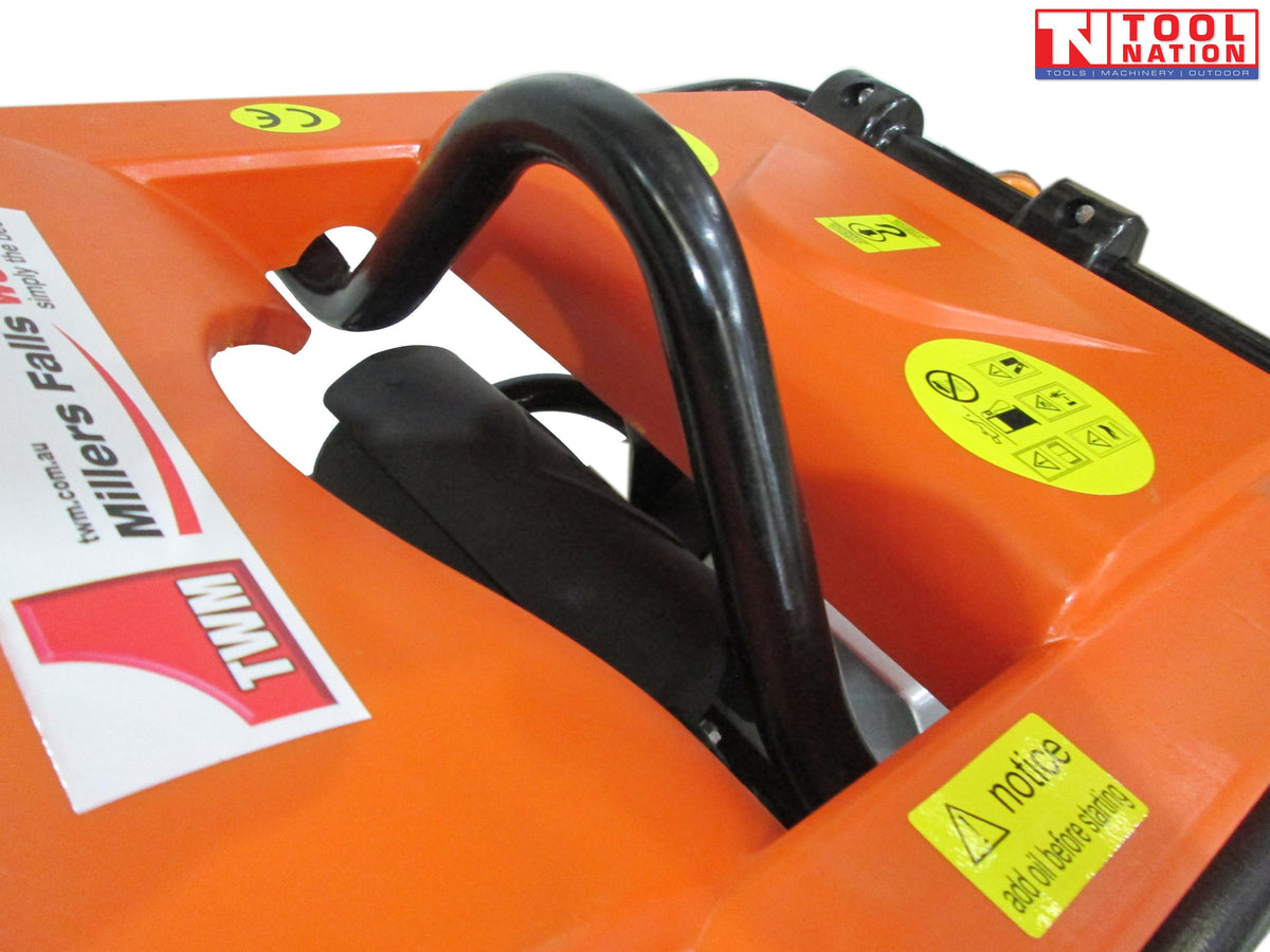 Close-up of an orange tamping rammer top cover with black handle, warning labels, visible branding, and logo in the top corner.