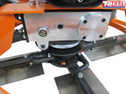 Close-up underneath an orange power trowel showing the gearbox housing, bolts, blade arms, and metal blades.