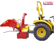 Red and yellow wood chipper attached behind a yellow tractor, with a feed hopper, curved discharge chute, rear wheel, and logo in the top right corner.