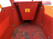 Inside view of a red feed hopper with wood chips on the floor, visible bolts, and a warning label on the centre panel.
