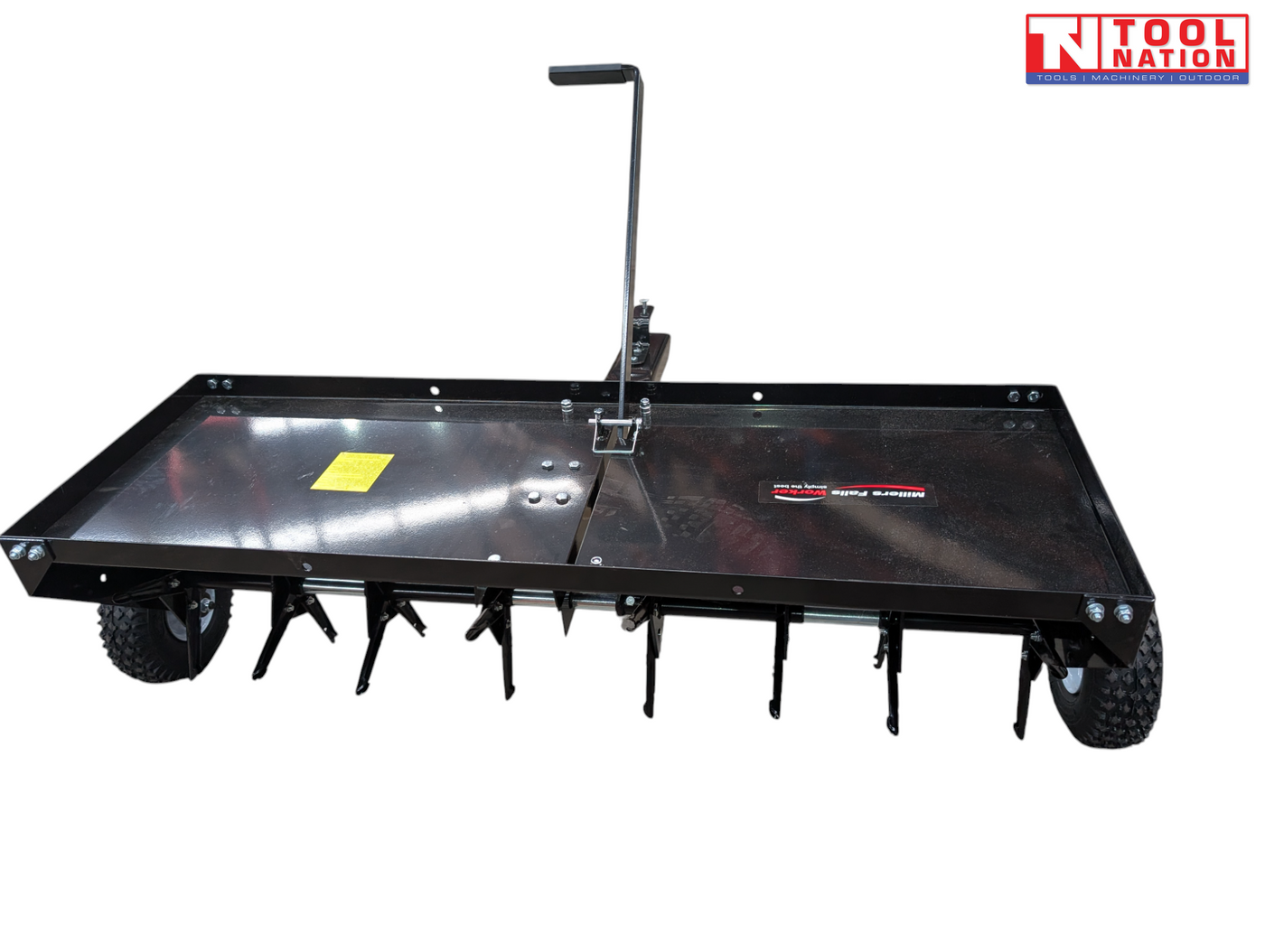 Black towable lawn aerator shown from the front with a tray, upright handle, two tyres and visible coring tines underneath.