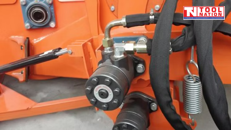 Close-up of hydraulic hoses, fittings, springs, and black cylindrical components mounted on an orange machine frame.