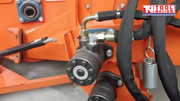 Close-up of hydraulic hoses, fittings, springs, and black cylindrical components mounted on an orange machine frame.