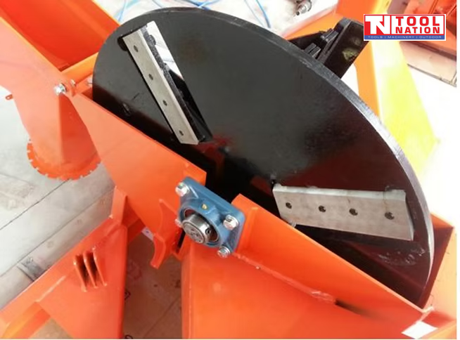 Close-up of a black internal chipper disc with metal blades, bolts, bearing housing, and orange machine panels.