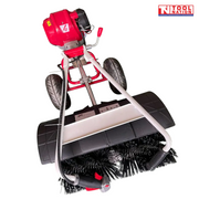 Close top view of a red and white walk-behind power broom showing the black brush bristles, black guard, two tyres, engine and handles.