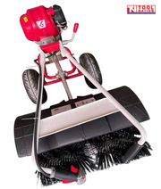 Close top view of a red and white walk-behind power broom showing black brush bristles, black guard, two tyres, engine and handles.