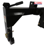 Close-up of a black quick hitch attachment showing a spring handle, side hook, pins, warning label, and a logo in the top right corner.