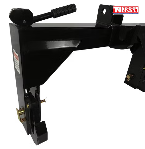 Close-up of a black quick hitch attachment showing a spring handle, side hook, pins, warning label, and a logo in the top right corner.