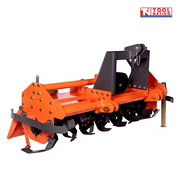 Rear angled view of an orange rotary tiller with black curved tines, black mounting frame, guard rail, support leg, bolts, and a logo in the top right corner.