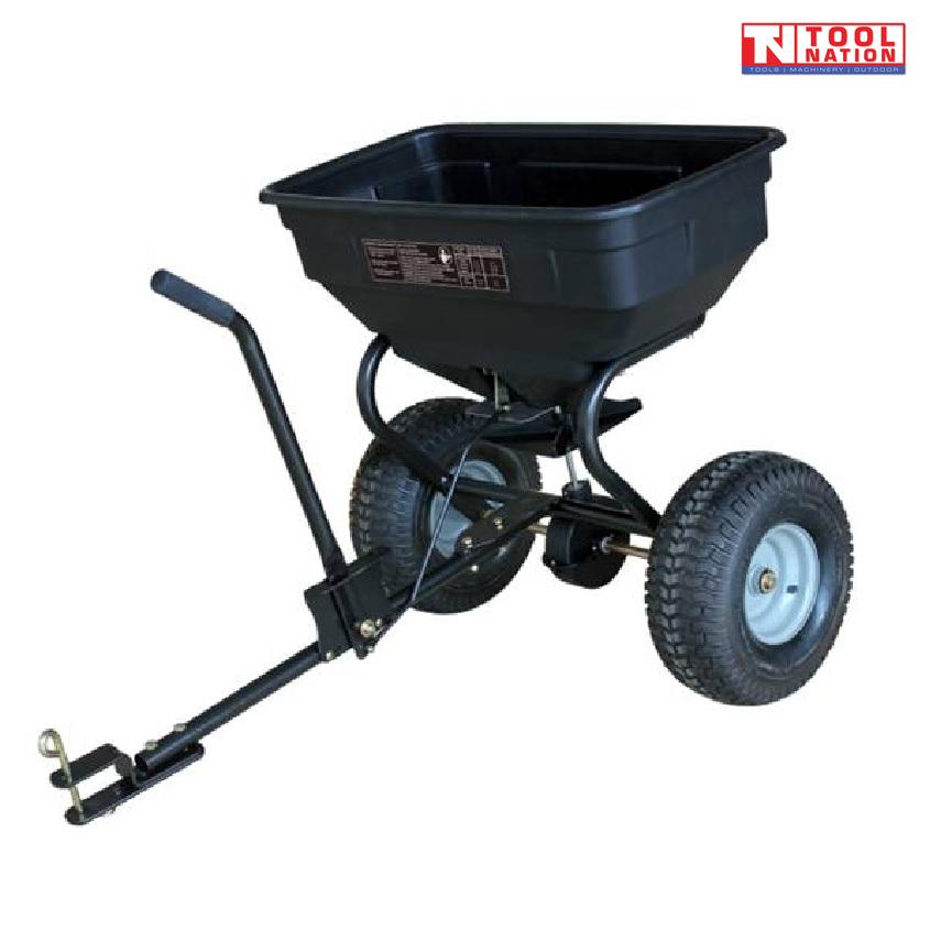 Black tow-behind spreader shown from the front side with an open hopper, long drawbar, upright handle, two treaded tyres and Tool Nation logo.