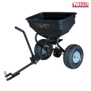 Black tow-behind spreader shown from the front side with an open hopper, long drawbar, upright handle, two treaded tyres and Tool Nation logo.
