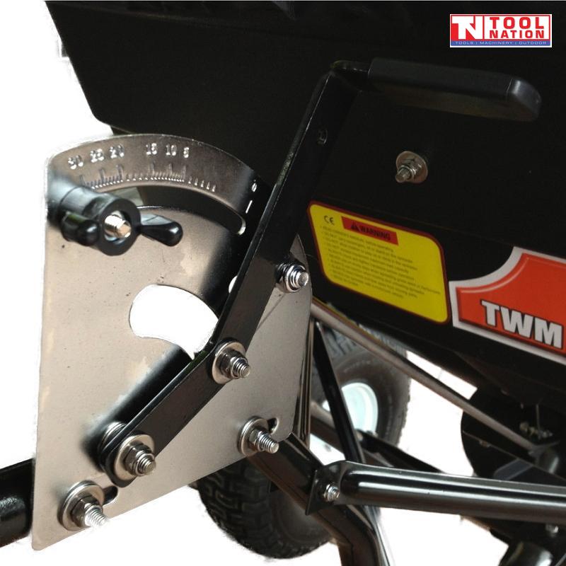 Close-up of a black tow-behind spreader showing a metal adjustment plate, black handle, bolts, warning label and part of a tyre.
