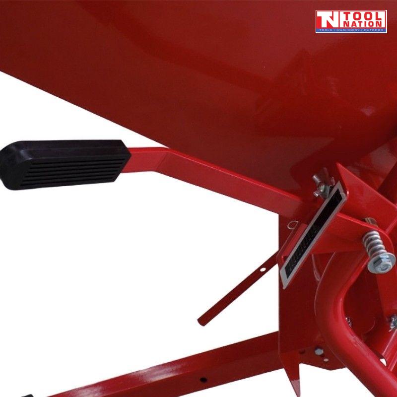 Close-up of a red tow-behind spreader showing a black handle grip, adjustment plate, spring, bolts and hopper side.