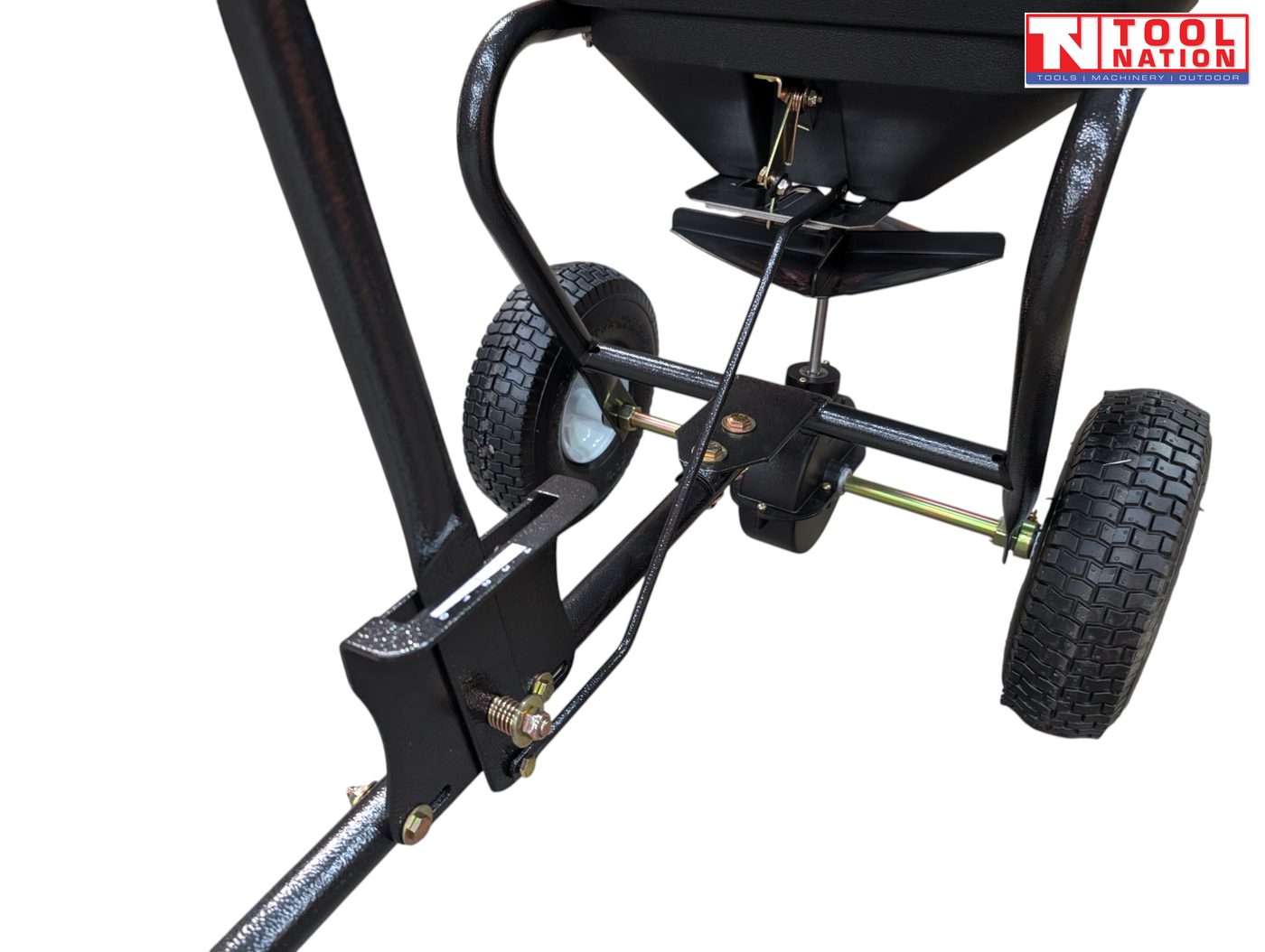 Close-up of a black walk-behind spreader showing the frame, axle, two treaded tyres, linkage and underside of the hopper.