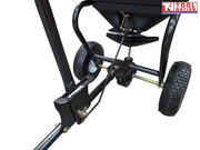 Close-up of a black walk-behind spreader showing the frame, axle, two treaded tyres, linkage and underside of the hopper.