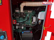 Internal view of the generator showing the engine, battery, coolant reservoir, and wiring inside the red enclosure.