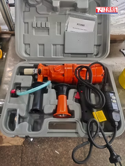 Orange handheld core drill inside an open grey carry case with power cord, side handle, hose, and switch box.