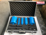 Open carry case containing blue core drill bits, metal adapters, drill bits, black foam insert, and logo in the top corner.