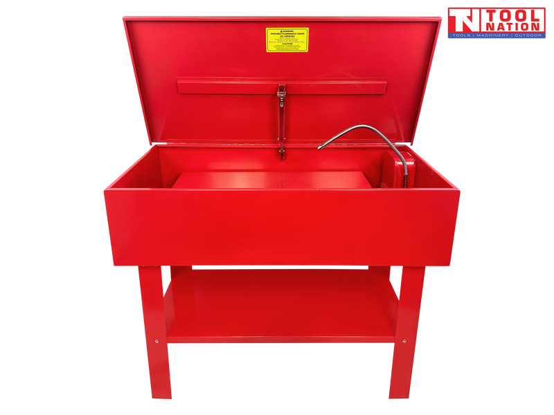 Red parts washer front view with lid open, flexible hose, yellow warning label, and lower shelf