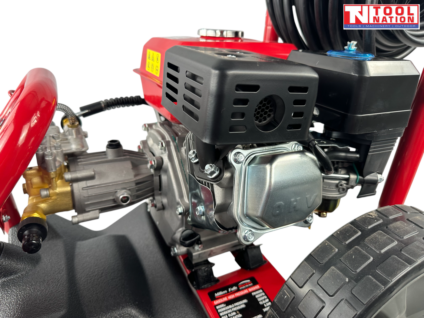 Close-up of a pressure washer engine and pump with black cover, brass fittings, large wheel, and a logo in the top right corner.