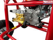 Close-up of a pressure washer pump, engine, brass fittings, red frame, wheel, and a logo in the top right corner.
