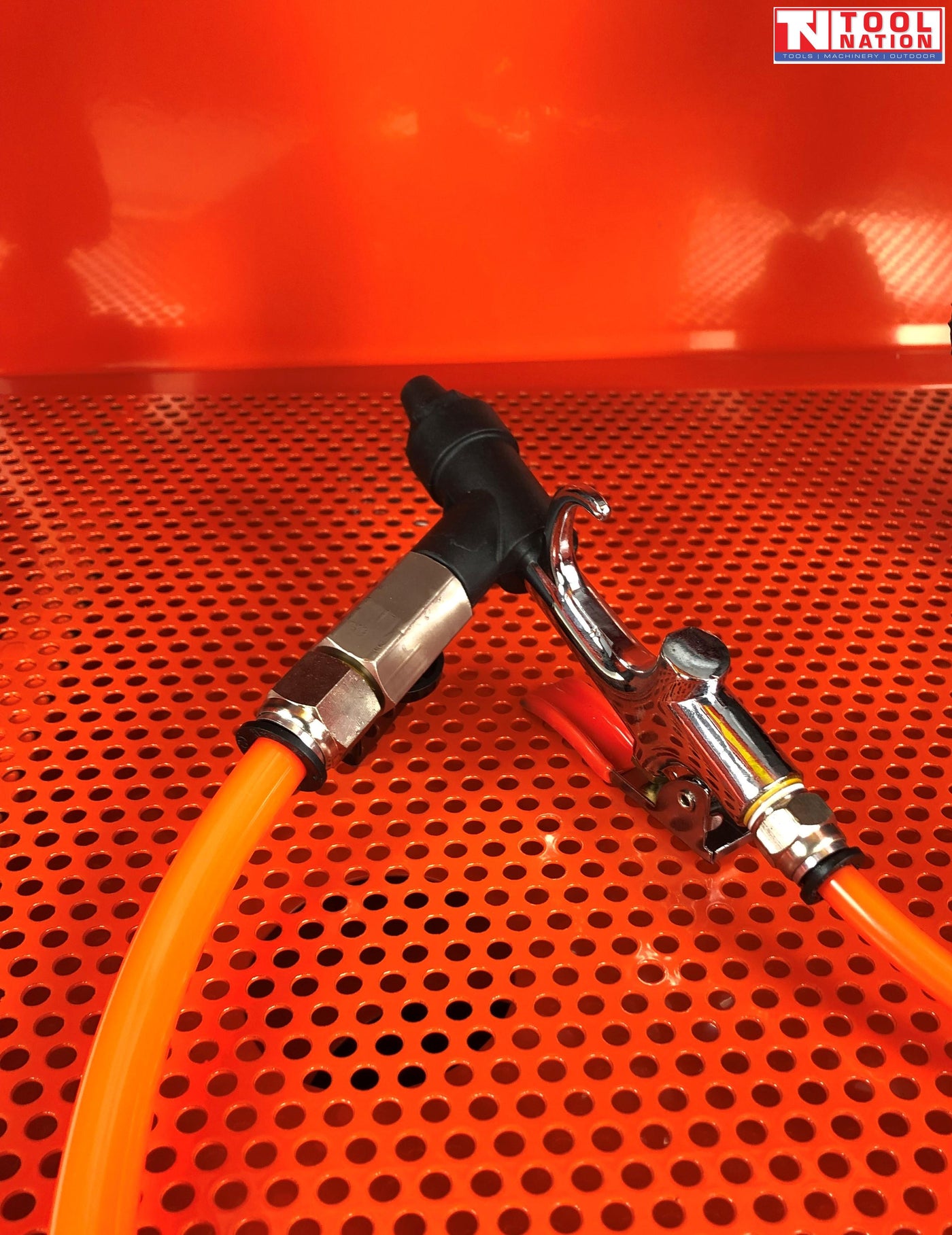 Close-up of spray gun with orange hose on perforated metal work surface