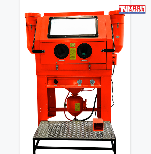 Front view of a large red sandblasting cabinet with a wide viewing window, two circular glove ports, lower pressure tank, hoses and a metal step platform.