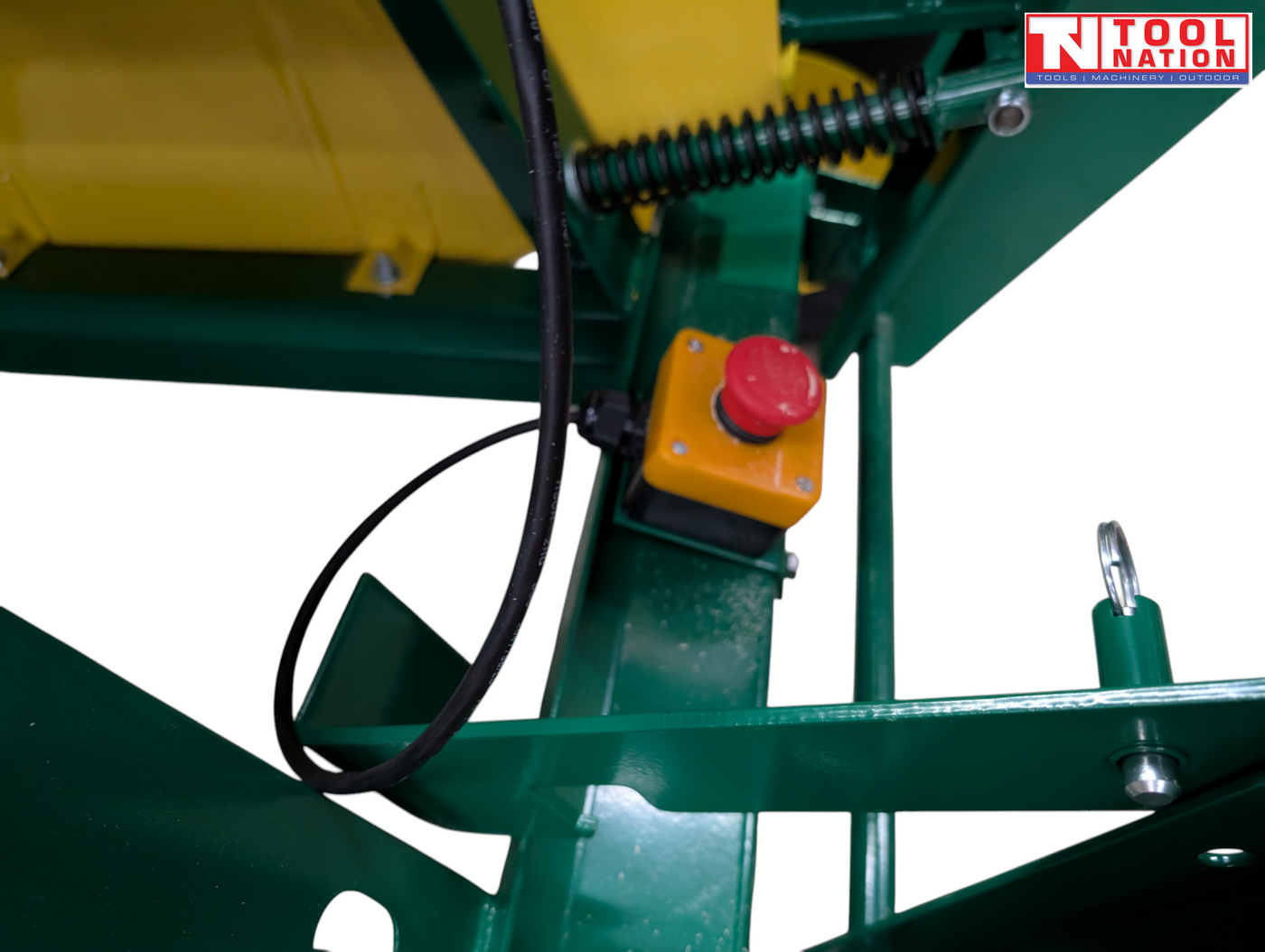 Close-up of a green and yellow saw bench frame showing a red emergency stop button, spring, cable and metal pin.