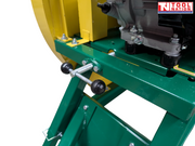 Close-up of a green saw bench frame showing a metal adjustment lever, bolts, yellow blade guard section and part of the engine.