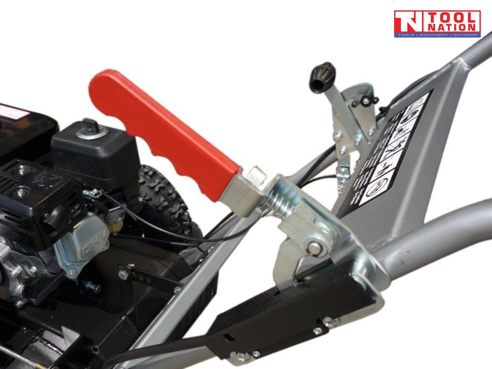 Close-up of a grey and black stump grinder showing a red lever, handle frame, warning label, engine area and part of a treaded tyre.