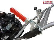 Close-up of a grey and black stump grinder showing a red lever, handle frame, warning label, engine area and part of a treaded tyre.