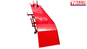 Front view of the red motorcycle lift with the loading ramp down, long platform, center service panel, and front wheel chock at the far end.