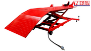 Angled front view of the raised red motorcycle lift with the loading ramp down, long platform, front wheel chock, and air hose.