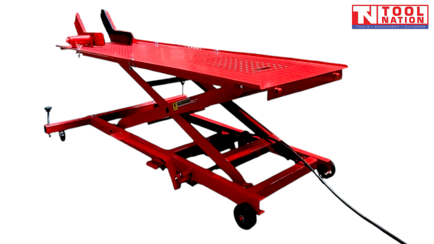 Angled front-side view of a red air hydraulic motorcycle lift with raised scissor frame, long platform, front wheel chock, and attached air hose.