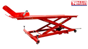Angled side view of a red motorcycle lift with the rear loading ramp down, front wheel chock raised, and scissor frame partially lifted.