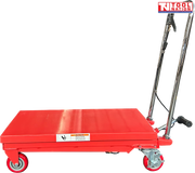 Side view of a red hydraulic lift table cart with lowered platform, chrome handle, wheels, and warning label.