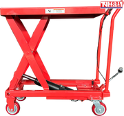 Side view of a red hydraulic lift table cart with raised scissor frame, handle, wheels, foot pedal, and warning label.
