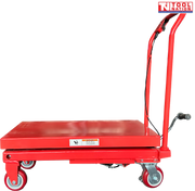 Side view of a red hydraulic lift table cart with lowered platform, handle, wheels, foot pedal, and warning label.
