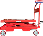 Side view of a red hydraulic lift table cart with lowered platform, handle, wheels, foot pedal, and warning label.